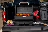 Parrilla portátil Masterbuilt montada en el platón de una camioneta, con comida lista