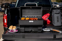 Parrilla portátil Masterbuilt montada en el platón de una camioneta, con comida lista
