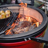 Churrasco y papas asándose sobre la parrilla del Kamado Joe con las llamas al fondo