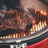Costillar ahúmandose sobre la parrilla de un Kamado Joe con las brasas al fondo