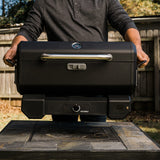 Hombre cargando la parrilla portátil Masterbuilt cerrada, tomada por sus asas laterales