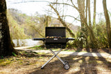 Parrilla portátil Masterbuilt armada junto a un río, con carne en la parrilla