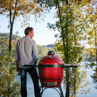 Pareja junto a un Kamado Joe rojo en una terraza frente al lago