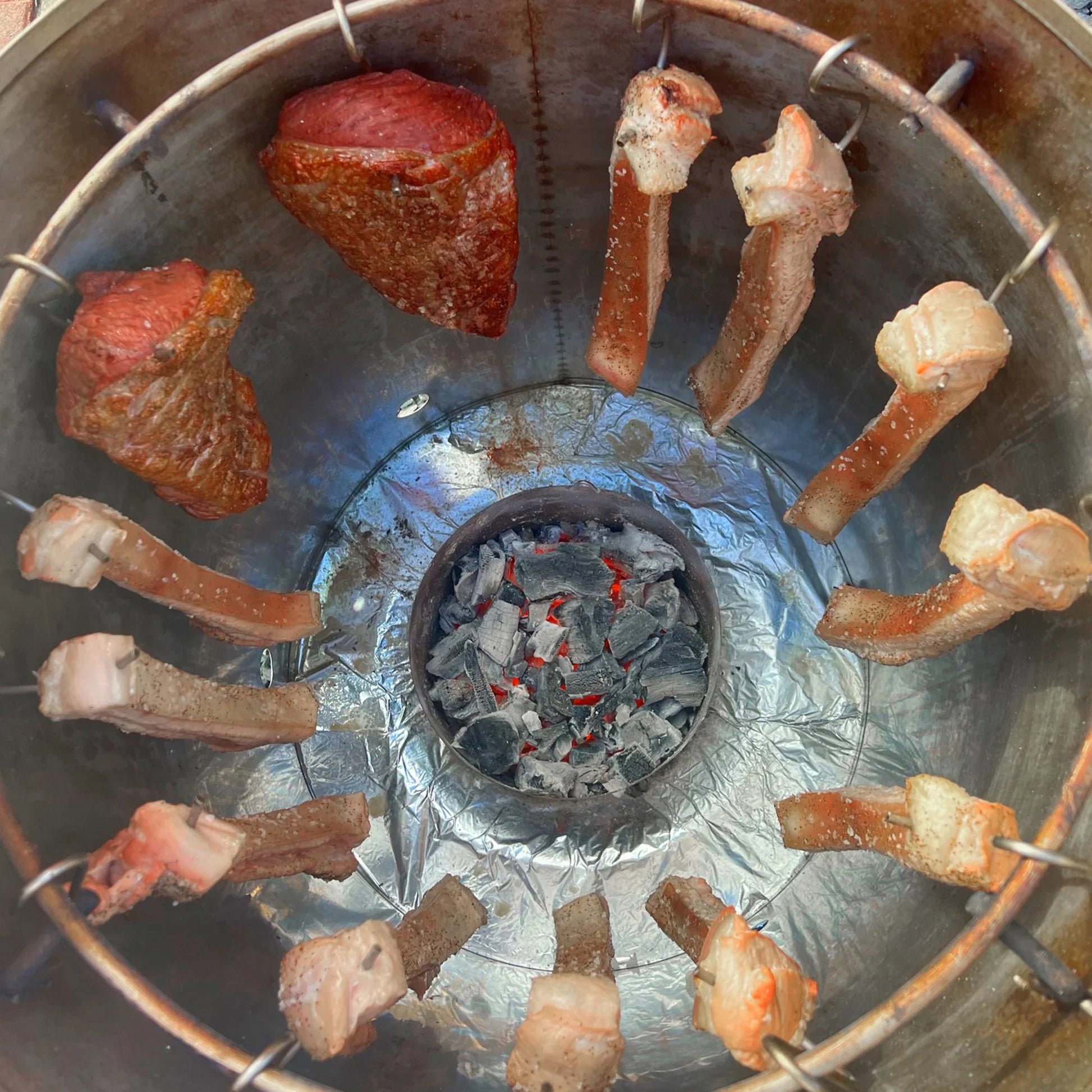 Carne y costillas asándose en barril asador jumbo de acero inoxidable con carbón encendido