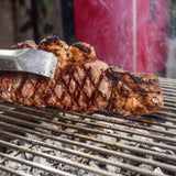 Corte de carne asándose a la parrilla sobre carbón, ideal para asados y BBQ.